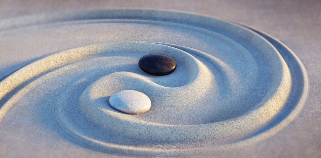 Symbole du yin et du yang dessiné dans le sable à l'aide de pierres noires et blanches